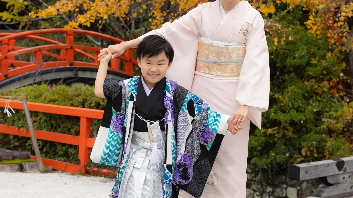紅葉の中、七五三の羽織袴姿の男の子と母親が神社の境内で微笑む写真
